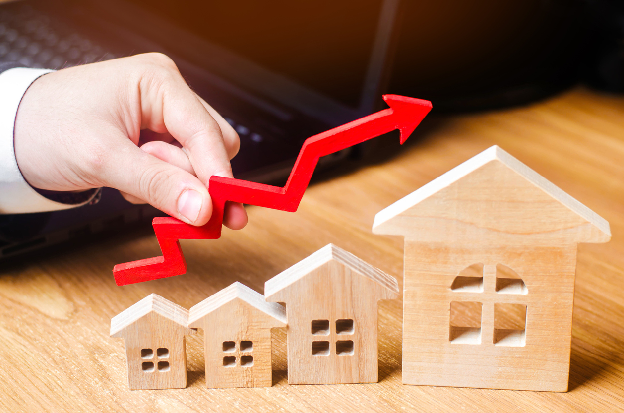 Wooden houses stand in a row from small to large with a red arrow up. concept of high demand for real estate. increase energy efficiency of housing. rise in house prices. property. businessman's hand