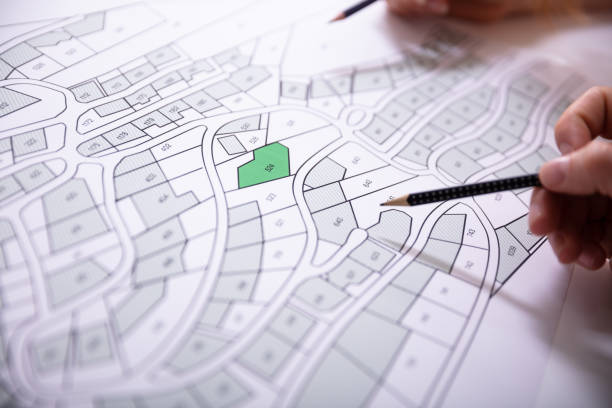 Close-up Of Human Hand Holding Pencil Over Paper Cadastre Map