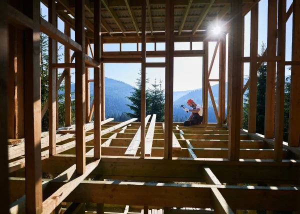 Carpenter constructing wooden frame, two-story house near forest