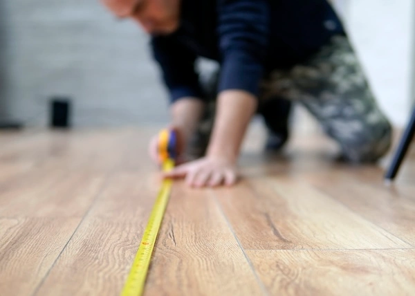 A worker measuring the length of a room's floor